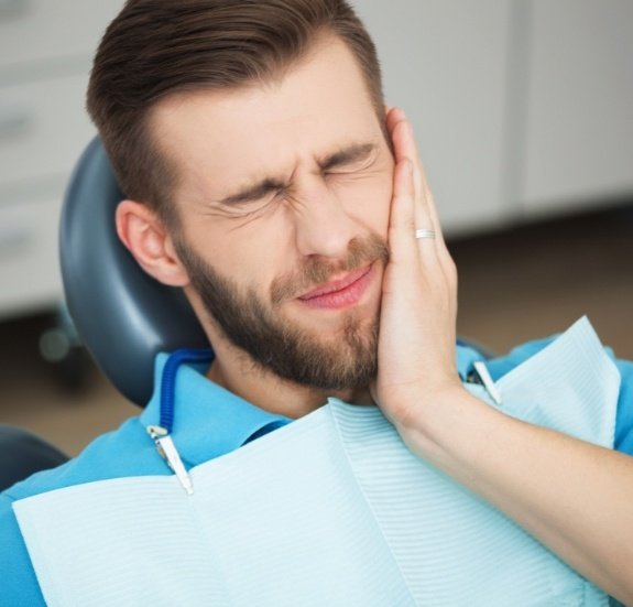 Man in dental chair holding the side of his face in pain