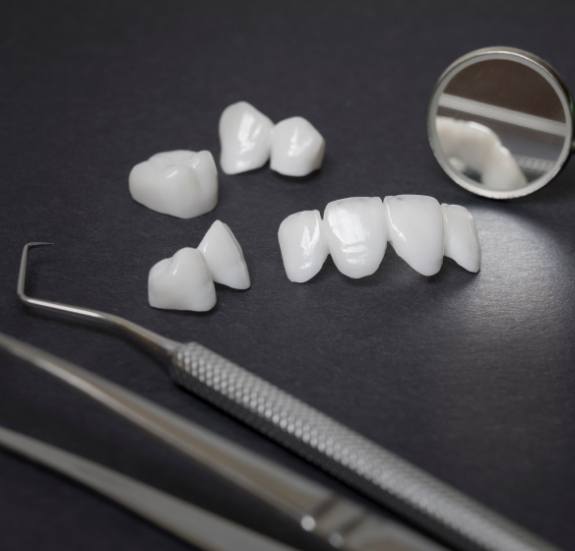 Several dental crowns and veneers on table next to dental instruments
