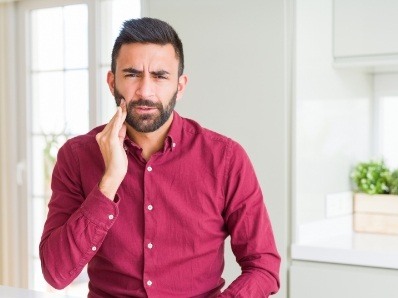 Man in red button up shirt holding his cheek in pain