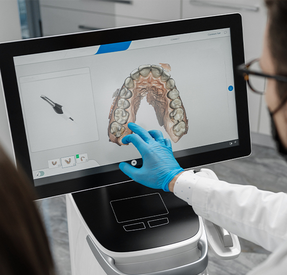 Dentist pointing to digital dental impressions of teeth on computer monitor