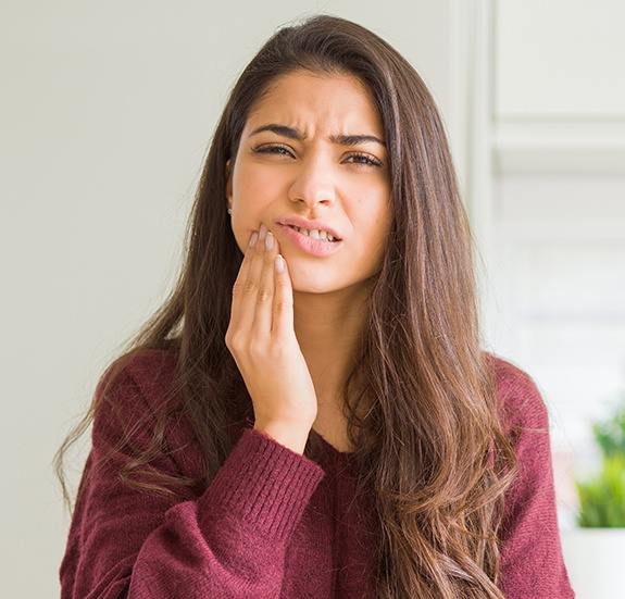 Woman in red sweater holding her cheek in pain