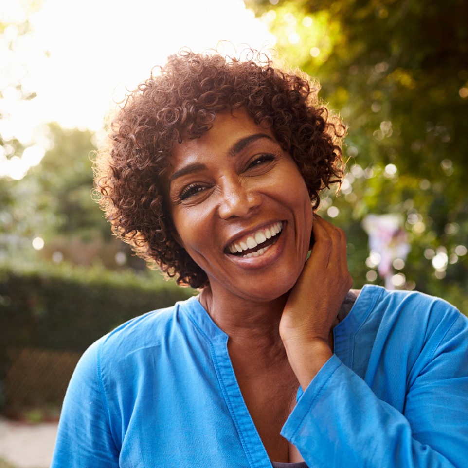 Middle-aged woman in blue smiling with full arch implant restorations in Revere