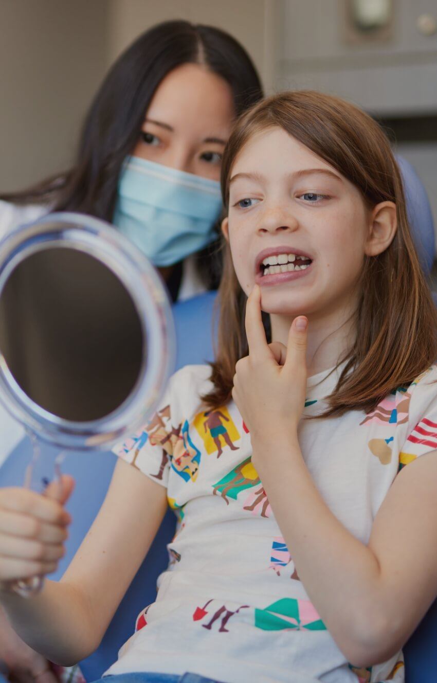 Young girl in dental chair looking at her smile in mirror