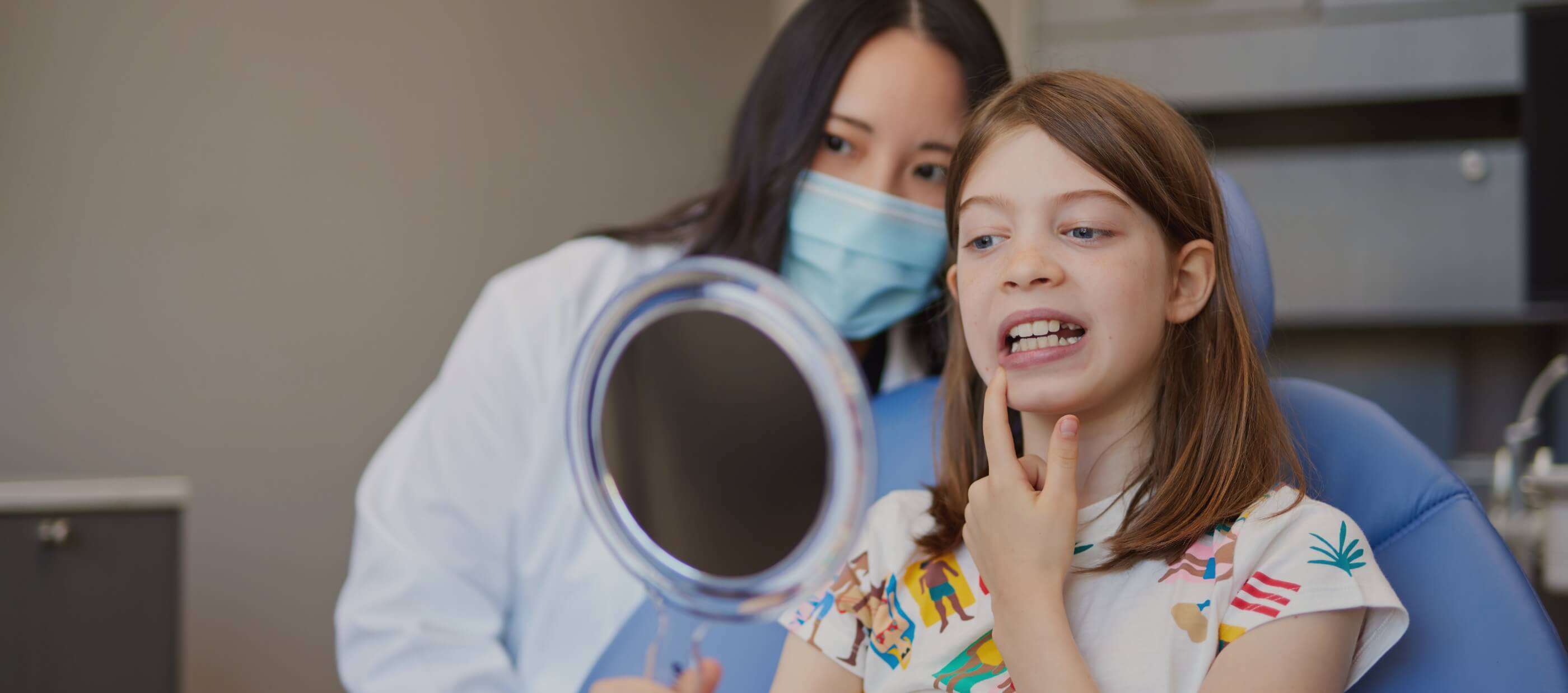 Young girl in dental chair looking at her smile in mirror