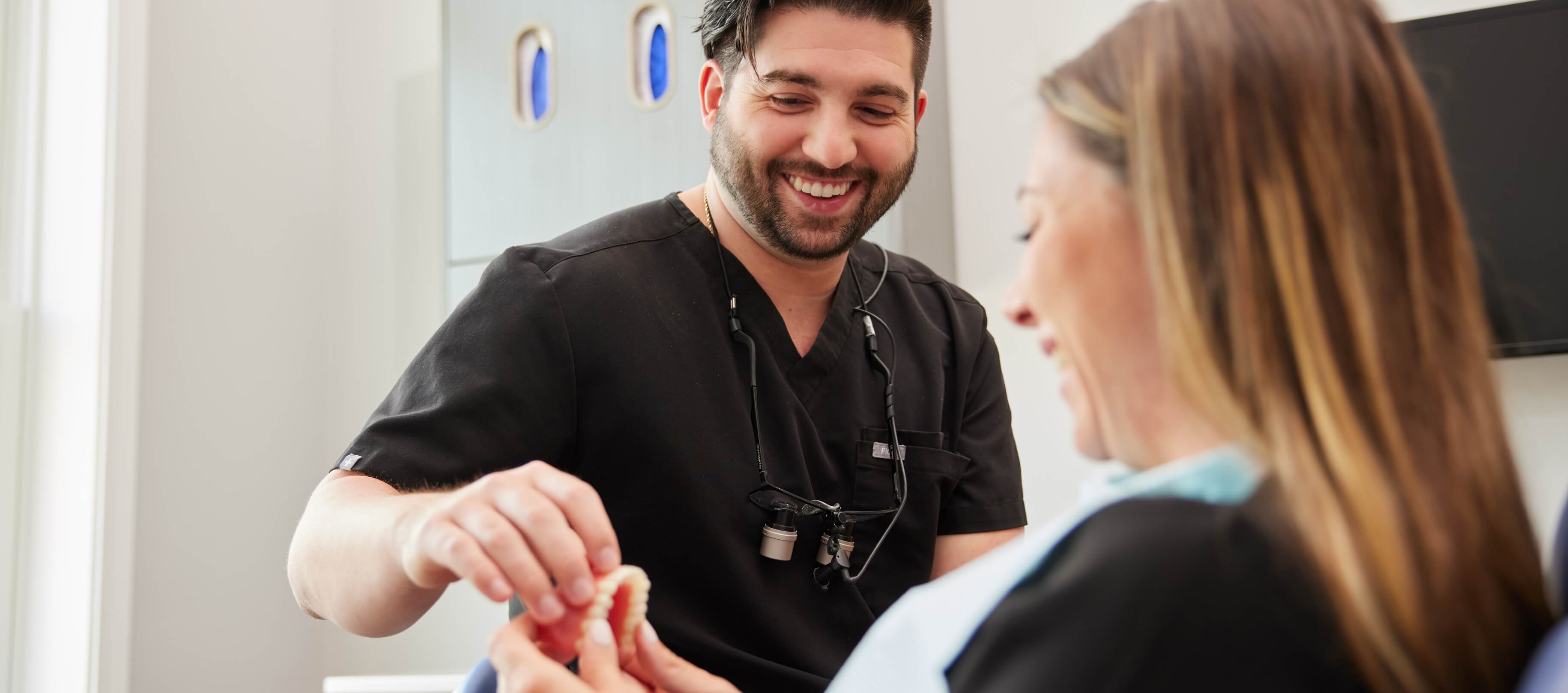 Doctor Adams smiling while showing a patient a model denture