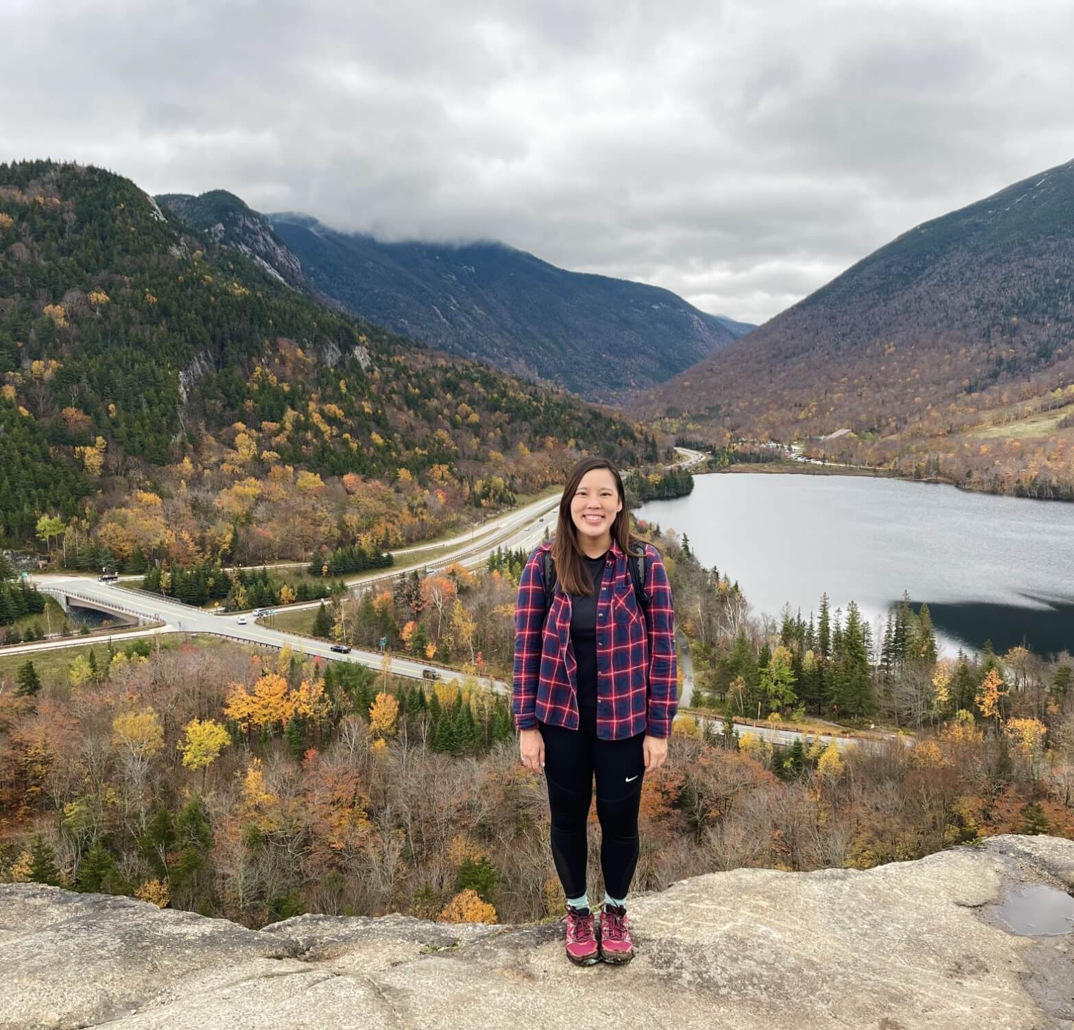 Doctor Ma standing on top of small mountain with other mountains and road in background