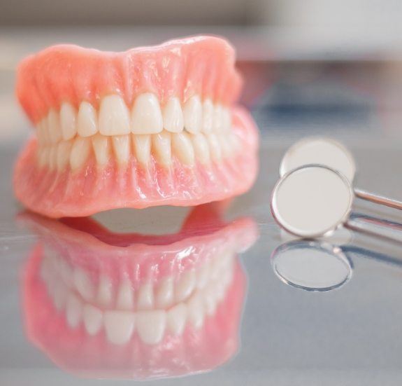 Set of full dentures on tray next to two dental mirrors