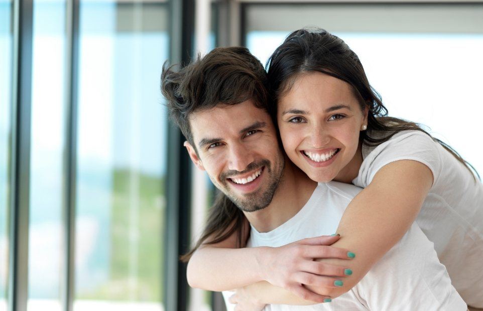 Smiling woman hugging smiling man from behind